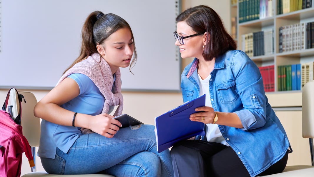 A high school student and a counselor having a supportive conversation in a bright room, demonstrating help-seeking in schools.