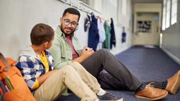 Teacher talking with a elementary aged student in a school hallway. 