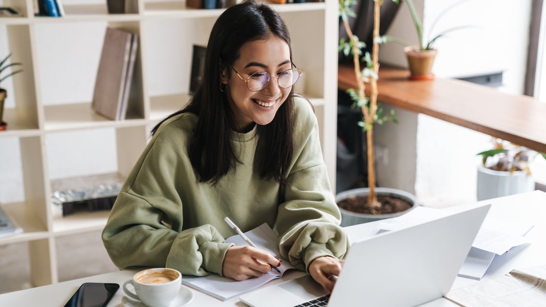 A school social worker smiles while using her laptop to explore free Tier-1 mental health resources inside a bright, welcoming office.