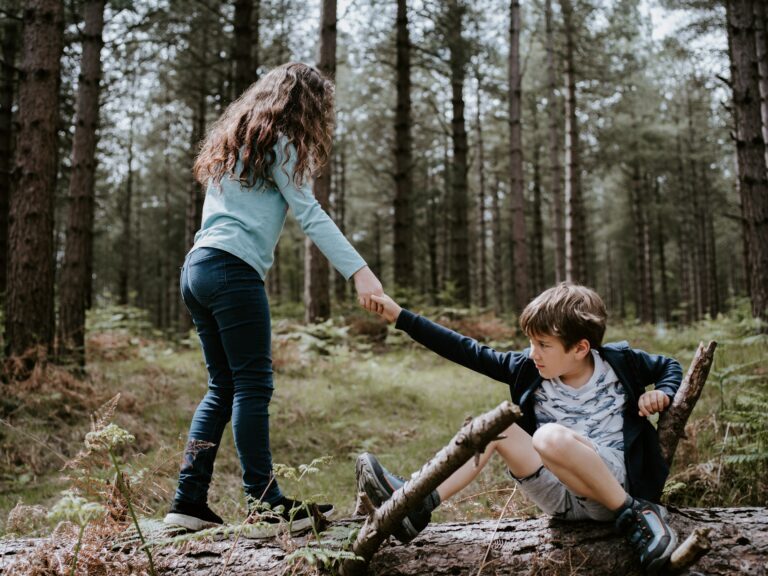 one adolescent helping the other up while playing in the woods